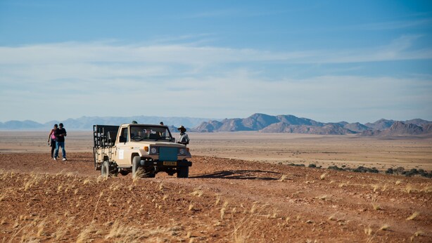 A desert landscape with a vehicle and two people. - Namib Desert Lodge (Sesriem)