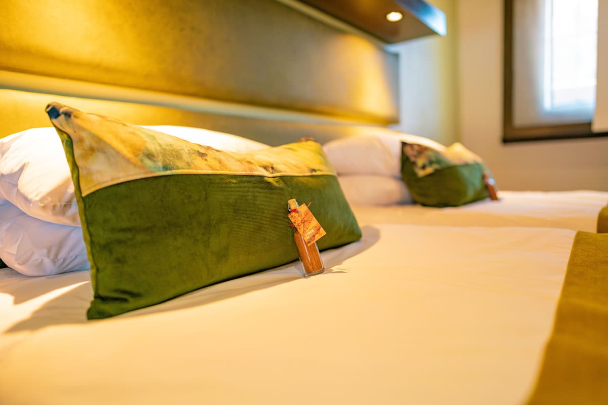 A hotel room with two beds, each with green pillows and a small decorative item on the pillows.
