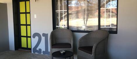 A room with two wicker chairs, a small round table, and a large window with a view of a desert landscape.