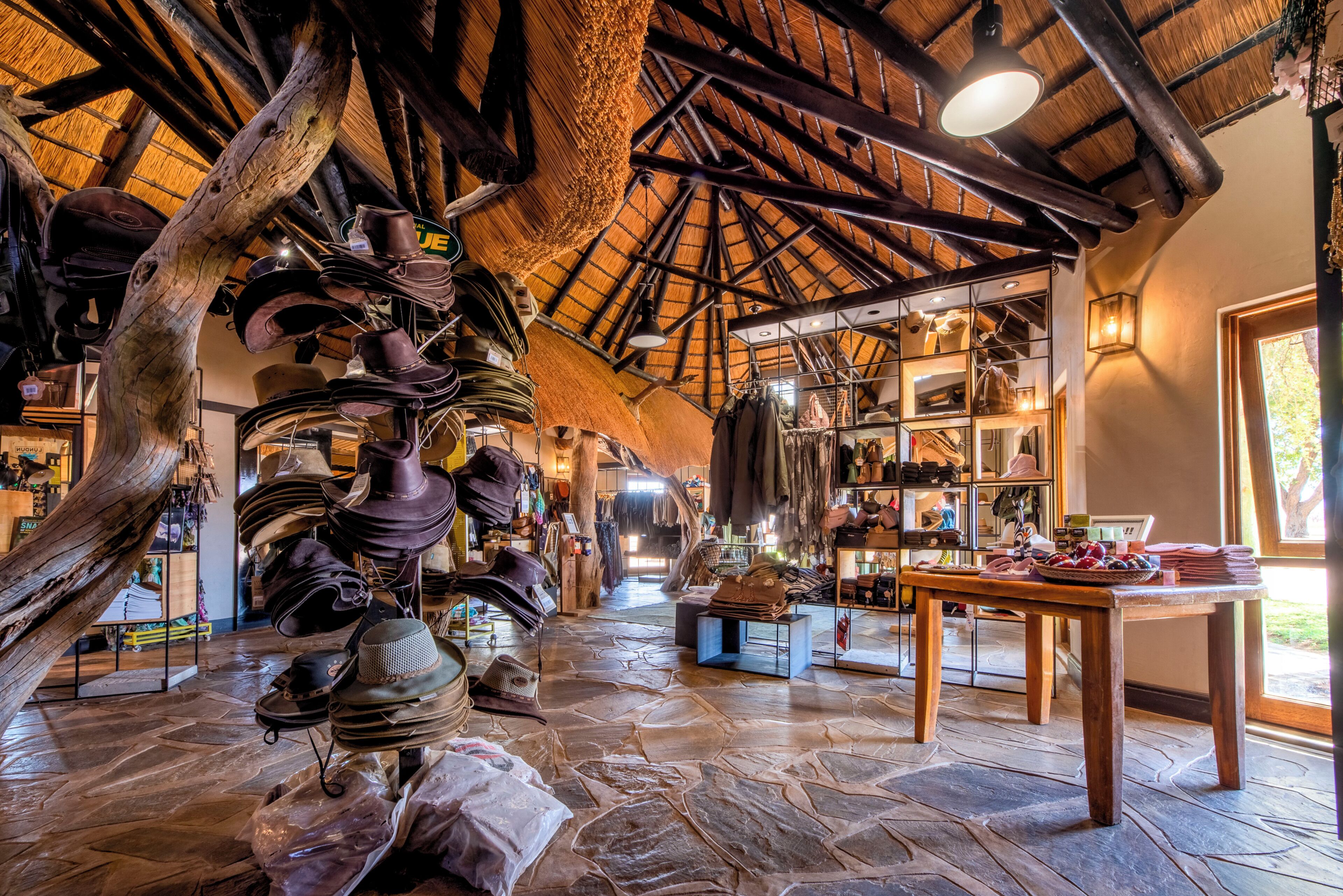 Un interior rústico con suelo de piedra, vigas de madera y varios sombreros y bolsos exhibidos en estantes y colgadores.