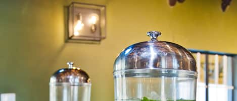 Dos dispensadores de bebidas con recipientes transparentes y hojas de menta, sobre una encimera de madera con una bandeja metálica.