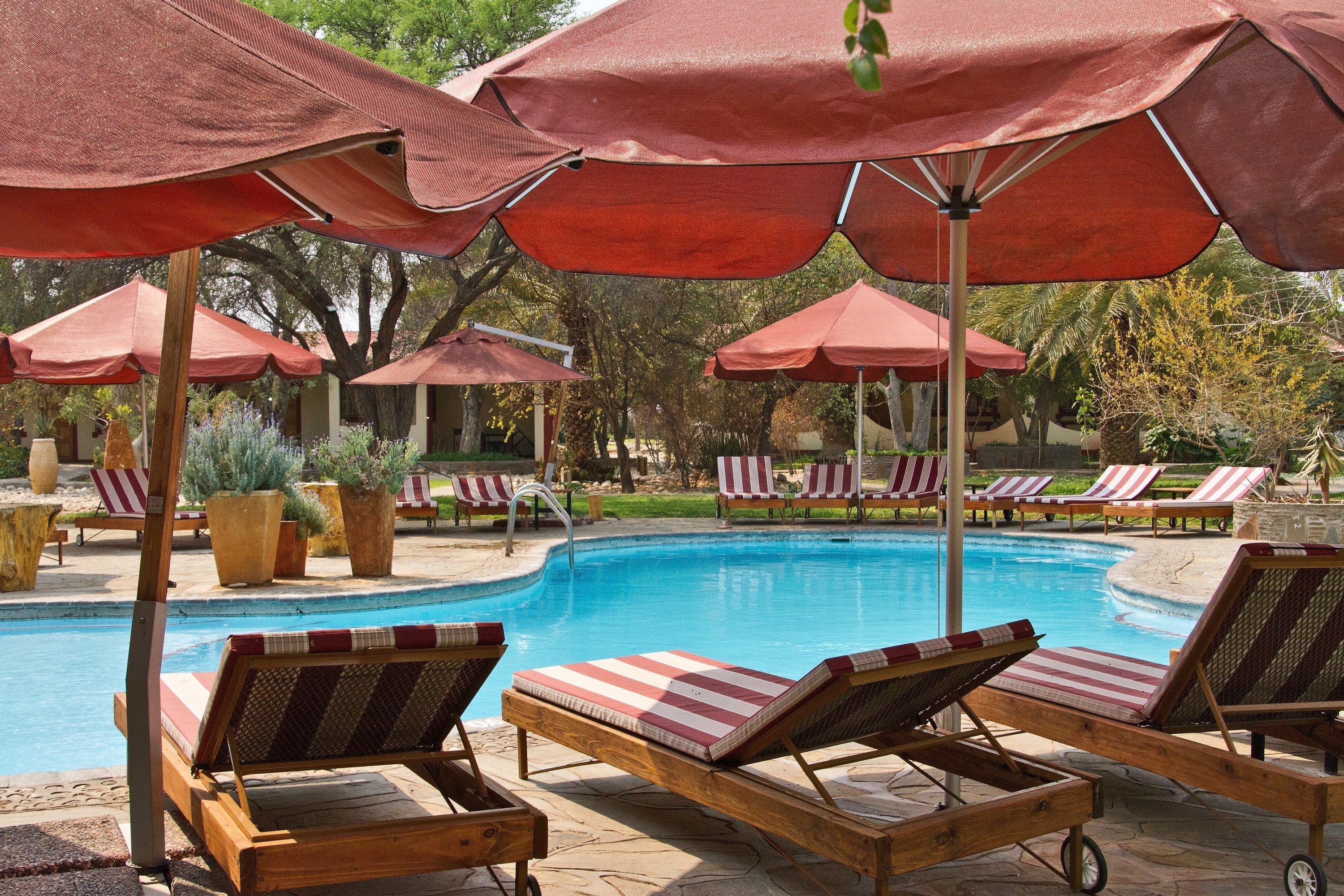 Zona de piscina con sillones de descanso y sombrillas rojas.