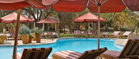 Zona de piscina con sillones de descanso y sombrillas rojas.