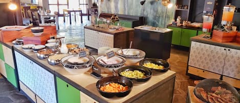 Un bufé con diversos alimentos y un área de descanso con sillas y mesas.