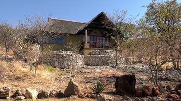 Un edificio rústico con techo de paja, muros de piedra y un balcón con vistas a un terreno pedregoso y vegetación escasa.