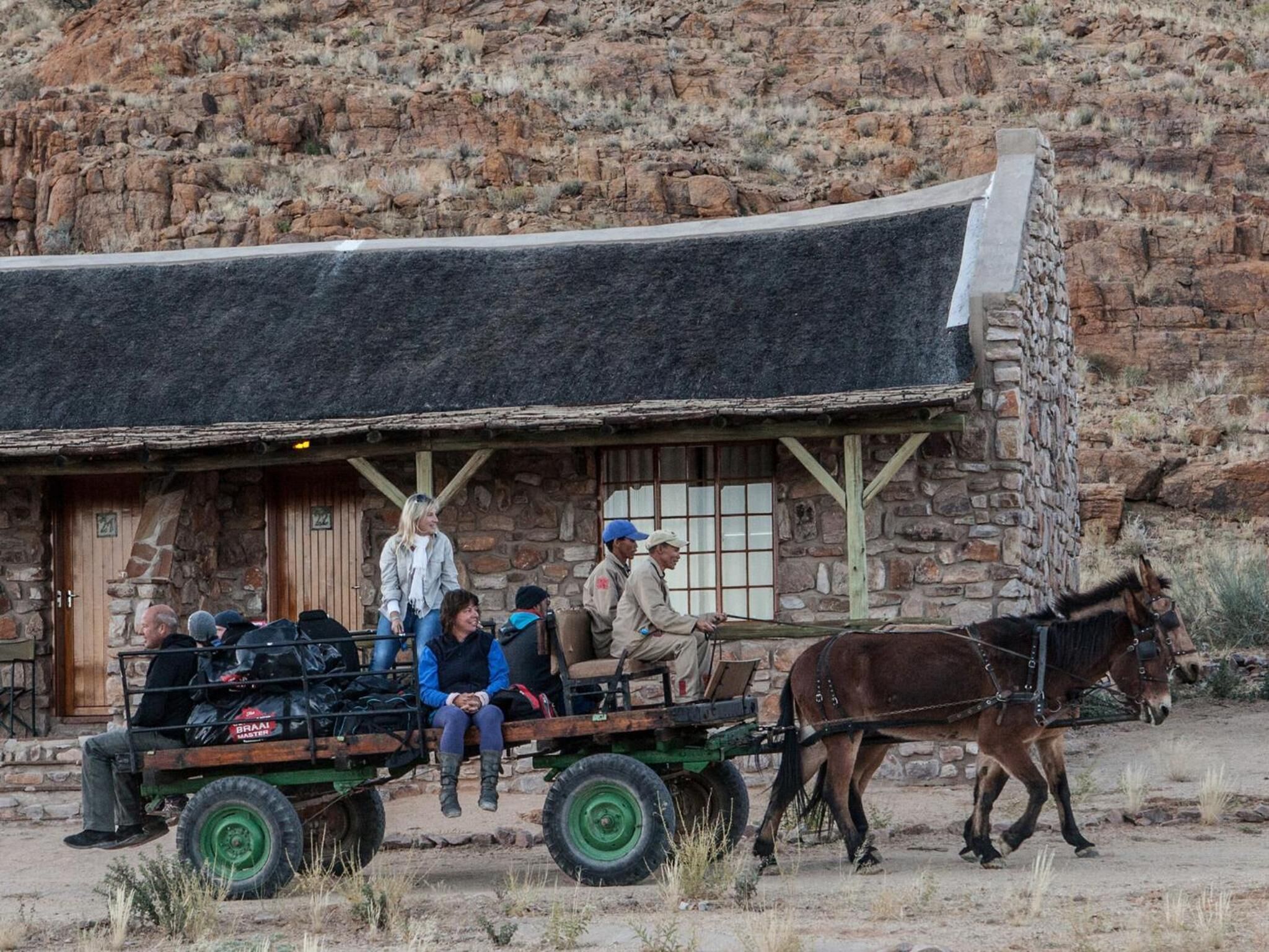 A rustic stone building with a thatched roof, a wooden cart with passengers, and a horse.