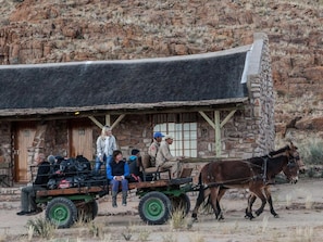 A rustic stone building with a thatched roof, a wooden cart with passengers, and a horse. - Canyon Village (Fish River Canyon)