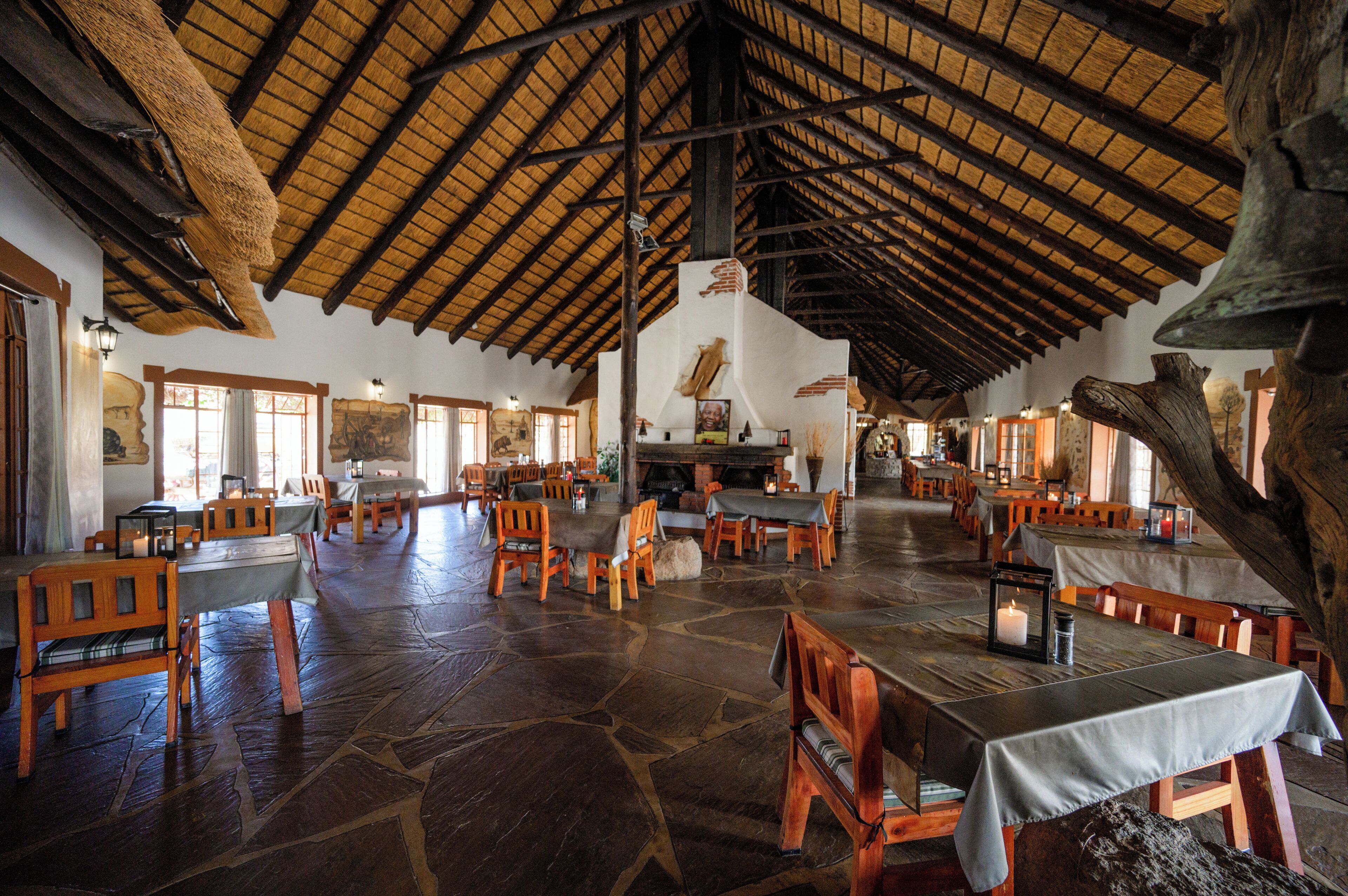 A spacious dining area with wooden tables and chairs, a stone floor, and a high wooden ceiling.