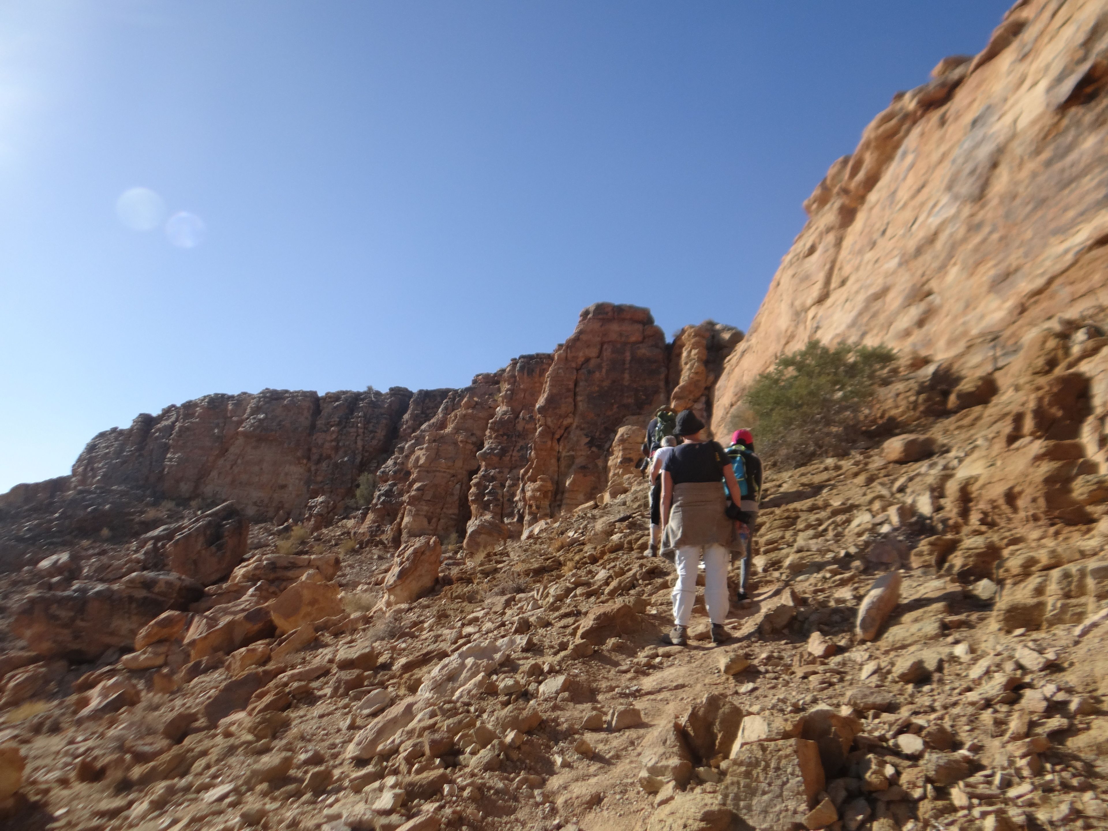 A rocky terrain with hikers ascending a steep, rugged cliff.
