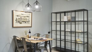 A dining area with a wooden table, metal chairs, a framed picture, pendant lights, and a black shelving unit with glass doors. - AinB Las Ramblas Colón Apartments (Barcelona)