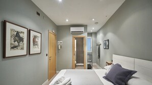A modern hotel room with a large bed, a wooden door, an air conditioning unit, and framed artwork on the wall. - AinB Las Ramblas Colón Apartments (Barcelona)