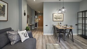 A modern living room with a grey sofa, a dining table with chairs, and a kitchen in the background. - AinB Las Ramblas Colón Apartments (Barcelona)