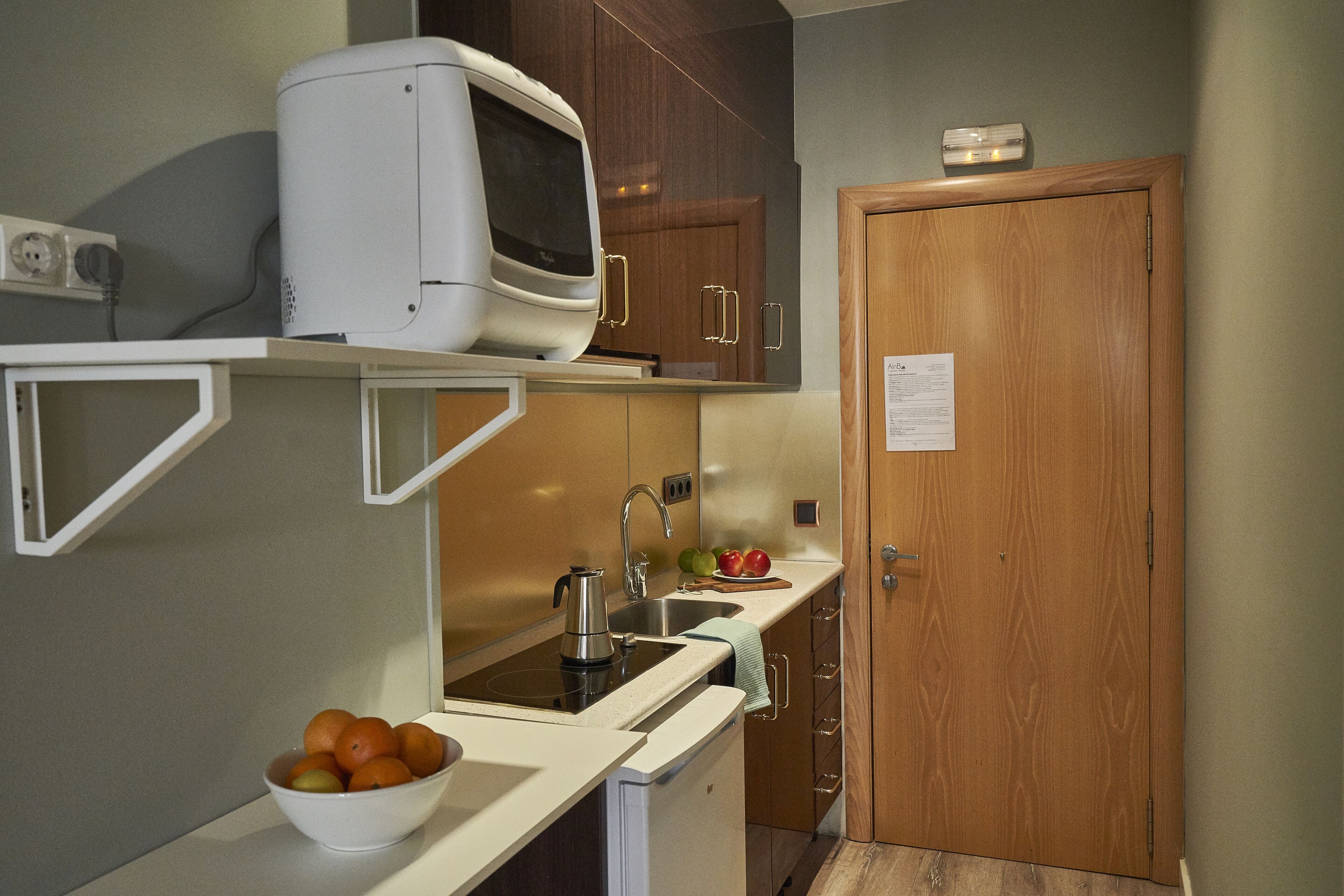 Een kleine keuken met een magnetron, spoelbak en een schaal fruit.