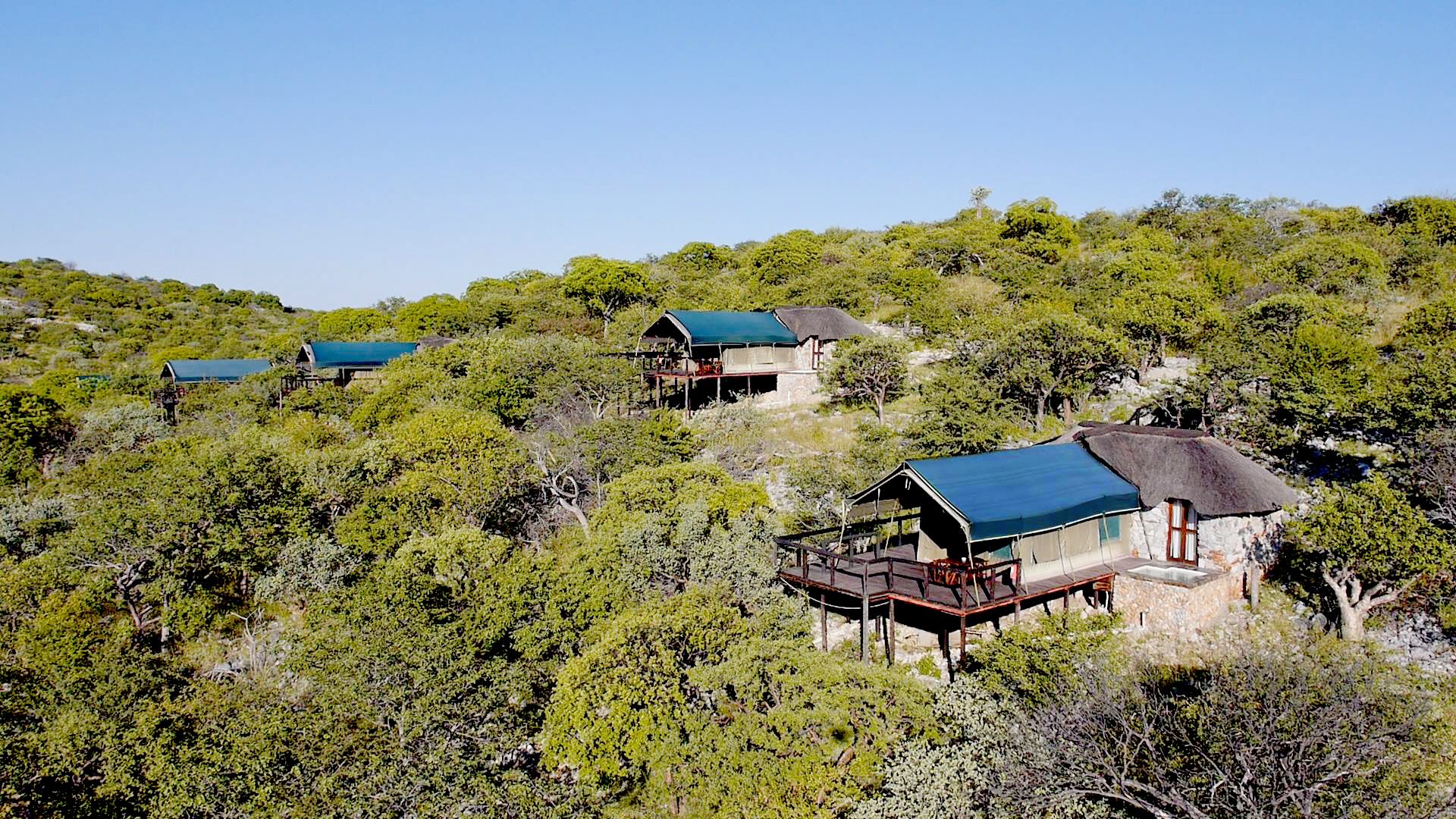 A hillside property with multiple buildings, each featuring a thatched roof and a balcony.