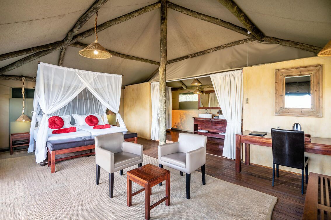 Una habitación con carpa, una cama, dos sillas, una mesita, un escritorio y un espejo.
