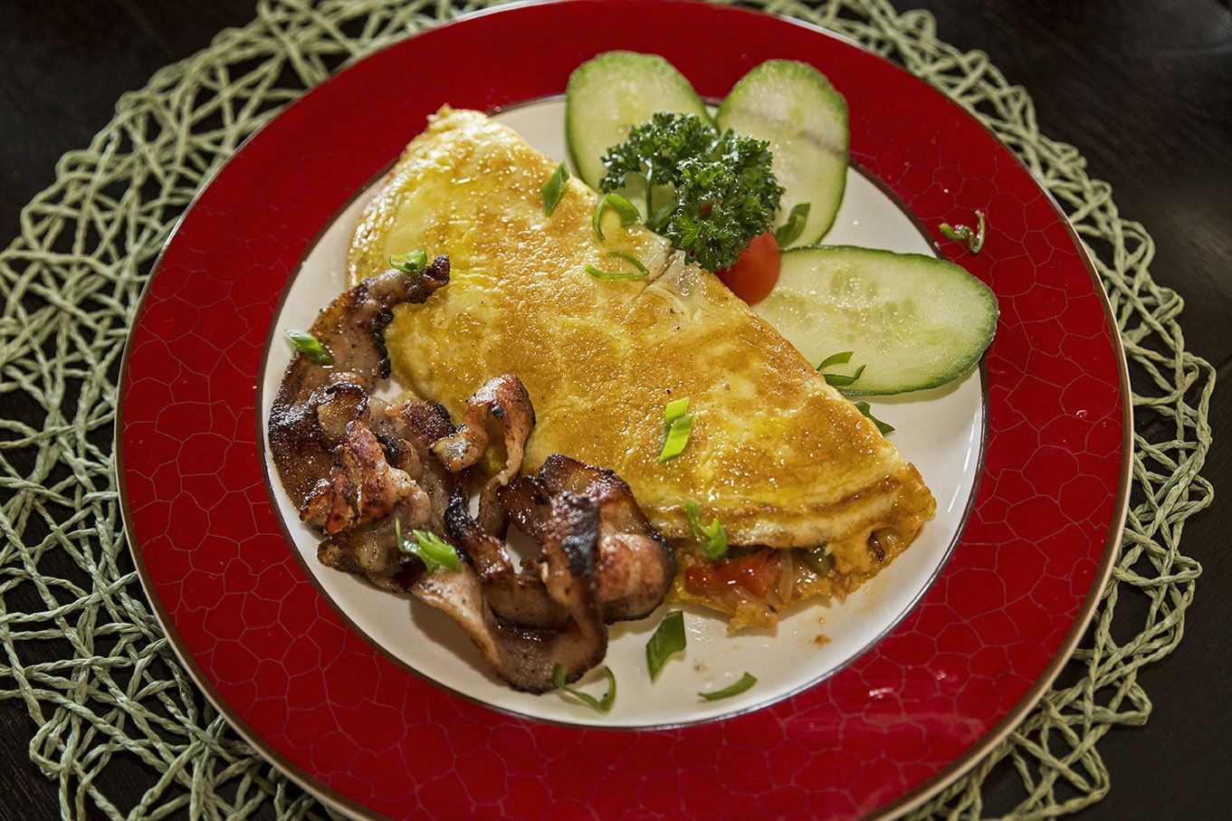 A plate with an omelette, mushrooms, and cucumber slices on a red plate.