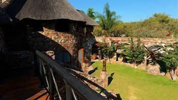 A stone building with a thatched roof, a wooden fence, and a well-maintained garden with various plants and a clear blue sky.