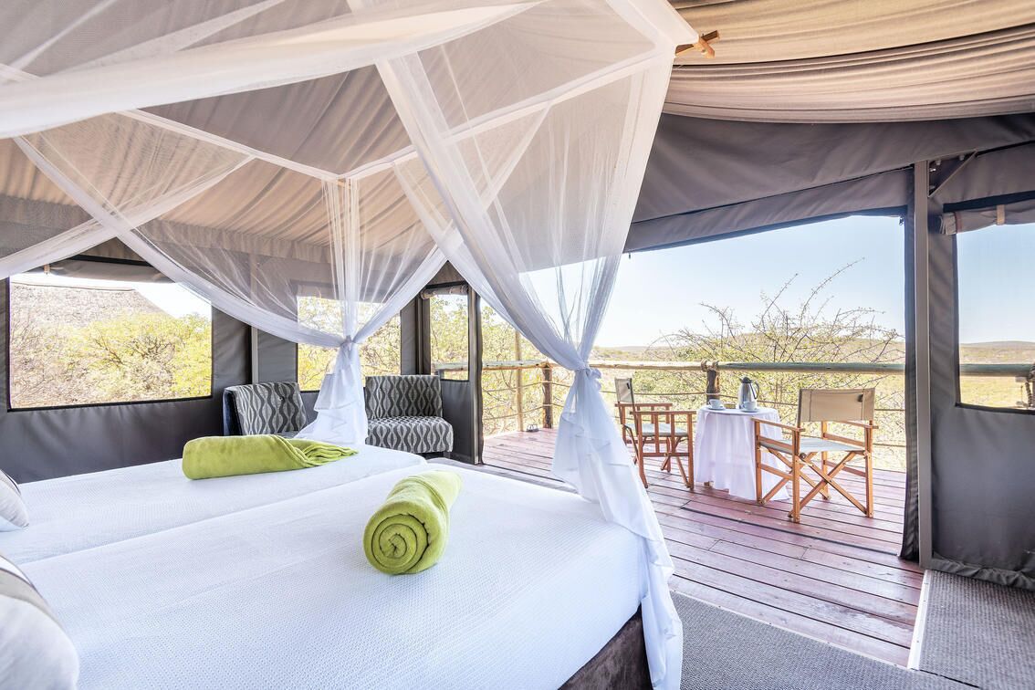 Una habitación con carpa, una cama, una mesa, sillas y vistas al exterior.