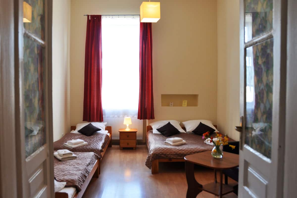 Une chambre d’hôtel avec deux lits simples, une petite table, une lampe et une fenêtre avec des rideaux.
