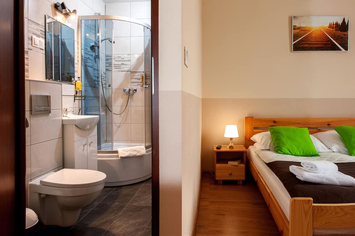 Une salle de bain avec des toilettes, un lavabo et une douche. La pièce est dotée d’un plancher en bois et d’un lit avec des oreillers verts.