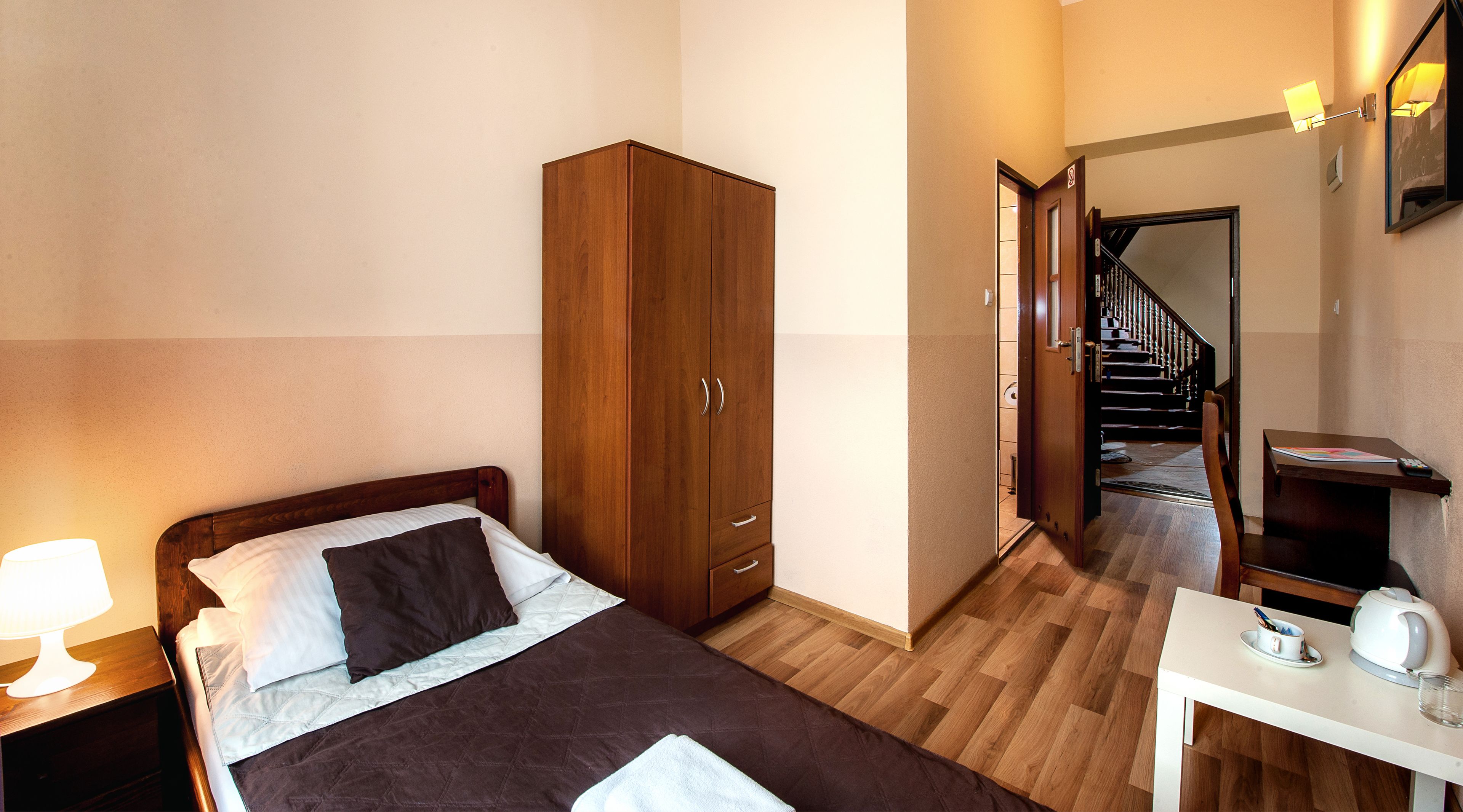 A bedroom with a bed, a wardrobe, a desk with a kettle, and a staircase leading to another room.