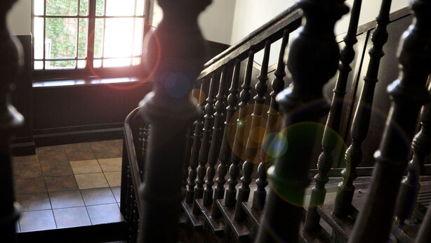 Una escalera de madera con barandilla que conduce a una habitación con ventana que deja entrar la luz del sol.