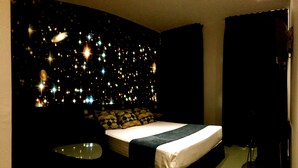 Une chambre d’hôtel moderne avec un grand lit, une table de chevet et un mur décoré d’un motif lumineux représentant des étoiles.