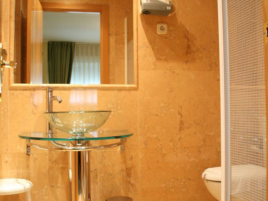 Ein Badezimmer mit einem Waschbecken aus Glas, einem Spiegel, einer Toilette und einer Duschkabine.