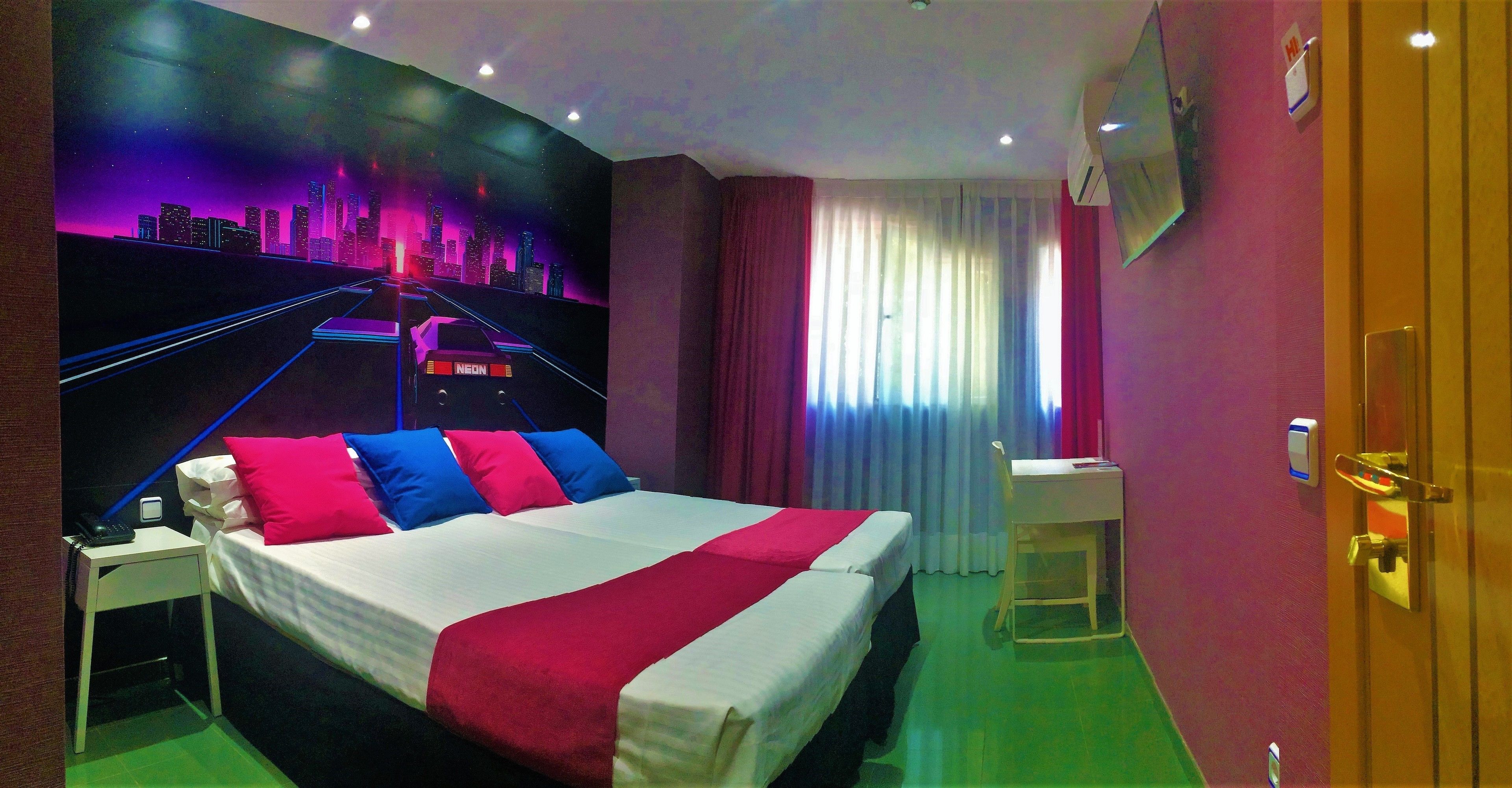 A hotel room with a bed, bedside table, and a cityscape mural on the wall.
