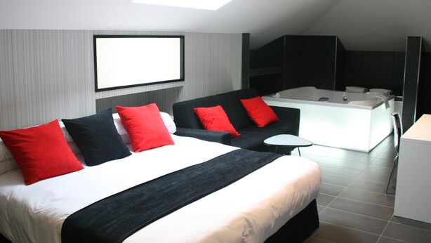 Une chambre d’hôtel moderne dotée d’un grand lit, d’un canapé, d’une petite table et d’une salle de bain séparée avec une baignoire.