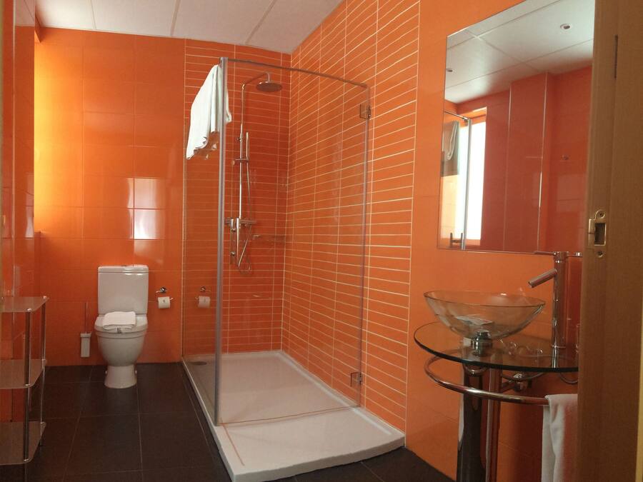 A bathroom with orange tiled walls, a glass shower enclosure, a white toilet, and a glass sink with a modern design.