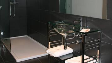 Un baño moderno con cabina de ducha de vidrio, lavamanos de vidrio y un perchero para toallas.