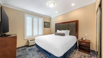 Una camera d'hotel con un letto grande, un comodino in legno, una televisione su un settimino e una finestra con persiane.