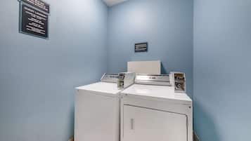 A laundry area with two washers and dryers, a sign detailing guest laundry hours and fees, and a small plaque on the wall.