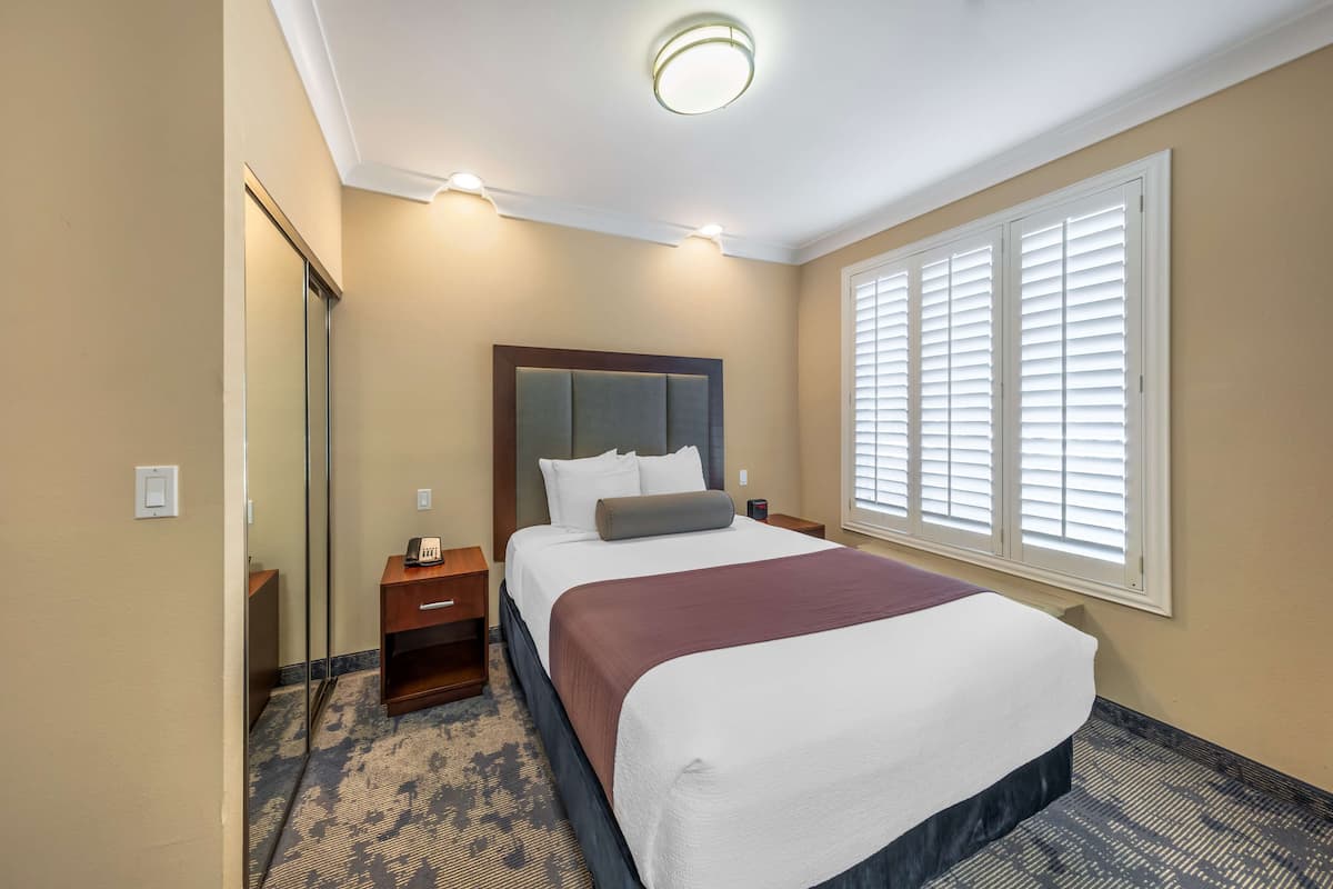 A hotel room with a large bed, a nightstand, a mirror, and a window with blinds.