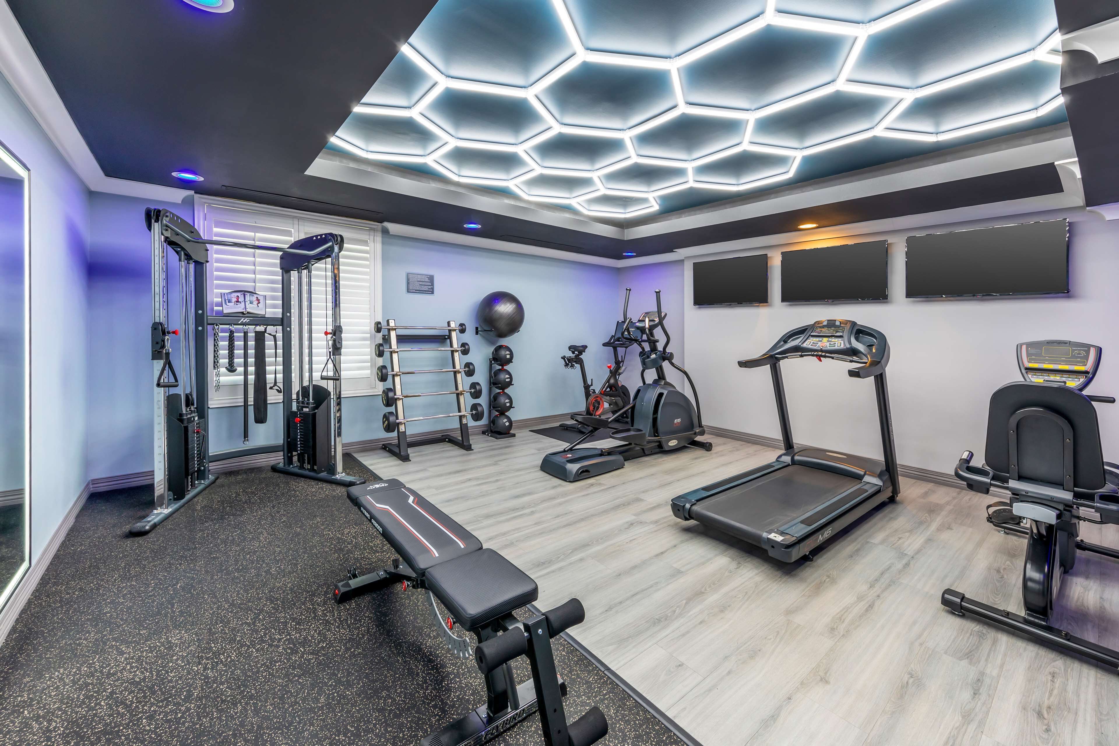 A modern gym with various exercise equipment, a bench, treadmills, and a hexagonal ceiling design.