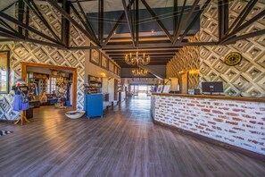 A spacious lobby with a wooden floor, a reception desk with a brick facade, and a patterned wall. - Etosha Safari Lodge (Okaukuejo)