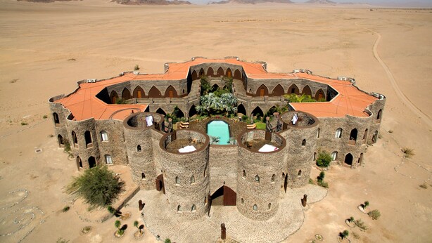 Un edificio grande y circular de piedra con techo rojo, rodeado por un paisaje desértico.