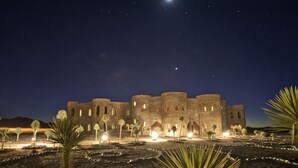 Un edificio histórico de piedra con múltiples arcos y un patio, iluminado por una luz ambiental nocturna.