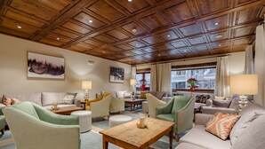 A spacious living room with a wooden ceiling, comfortable seating, and large windows offering a view of the outdoors. - Hotel Chalet Bassibe (Naut Aran)