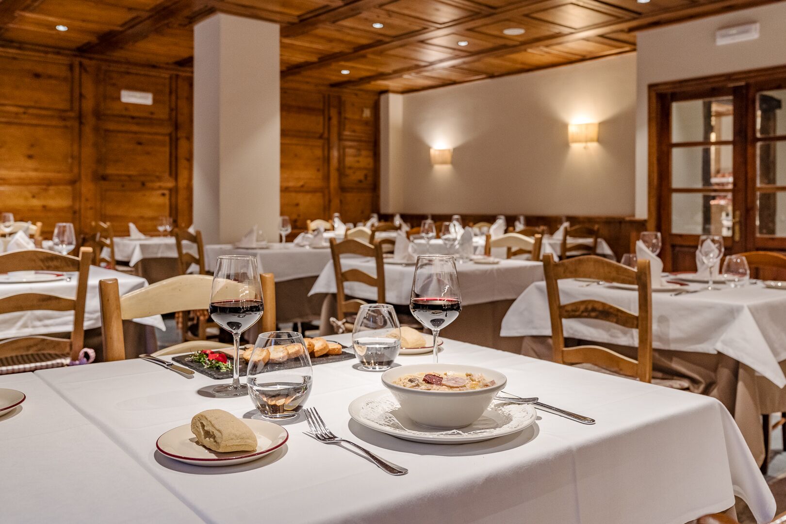 A restaurant with multiple tables set for dining, each with white tablecloths, wine glasses, and plates of food.