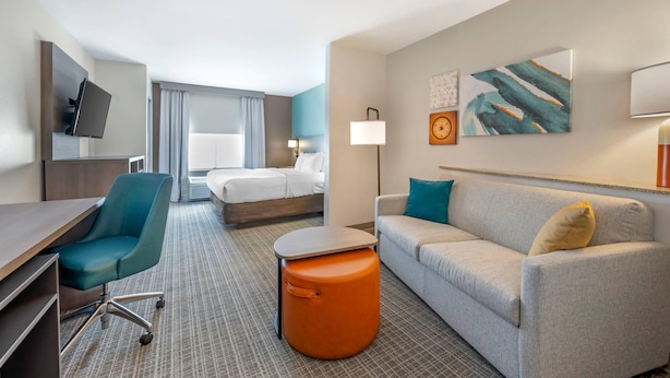 A hotel room with a desk, chair, sofa, ottoman, bed, and artwork on the wall. - Comfort Suites French Lick (French Lick)