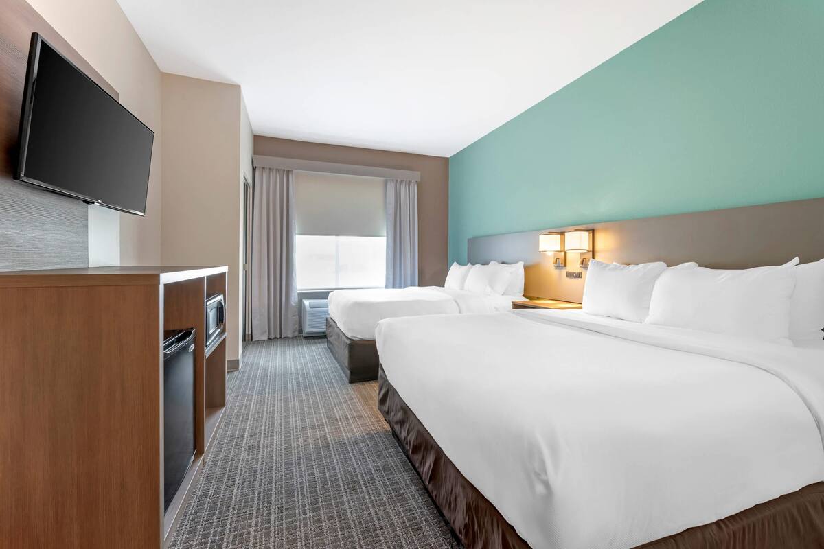 A hotel room with a large bed, a smaller bed, a desk with a TV, and a window with curtains.
