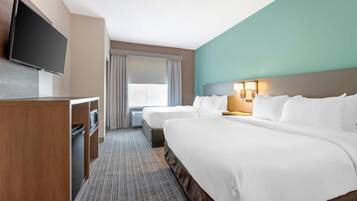 Een hotelkamer met een groot bed, een kleiner bed, een bureau met een televisie en een raam met gordijnen.
