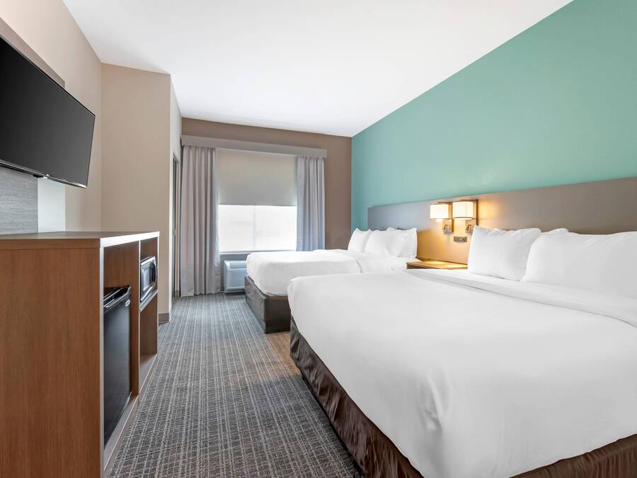 Een hotelkamer met een groot bed, een kleiner bed, een bureau met een televisie en een raam met gordijnen.
