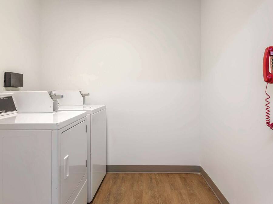 A laundry room with a washing machine, dryer, and a red telephone mounted on the wall.