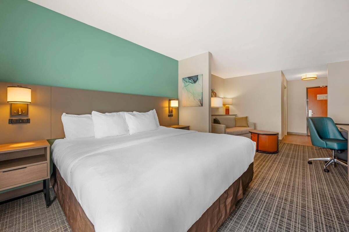 A hotel room with a large bed, a desk, a chair, and a small table.