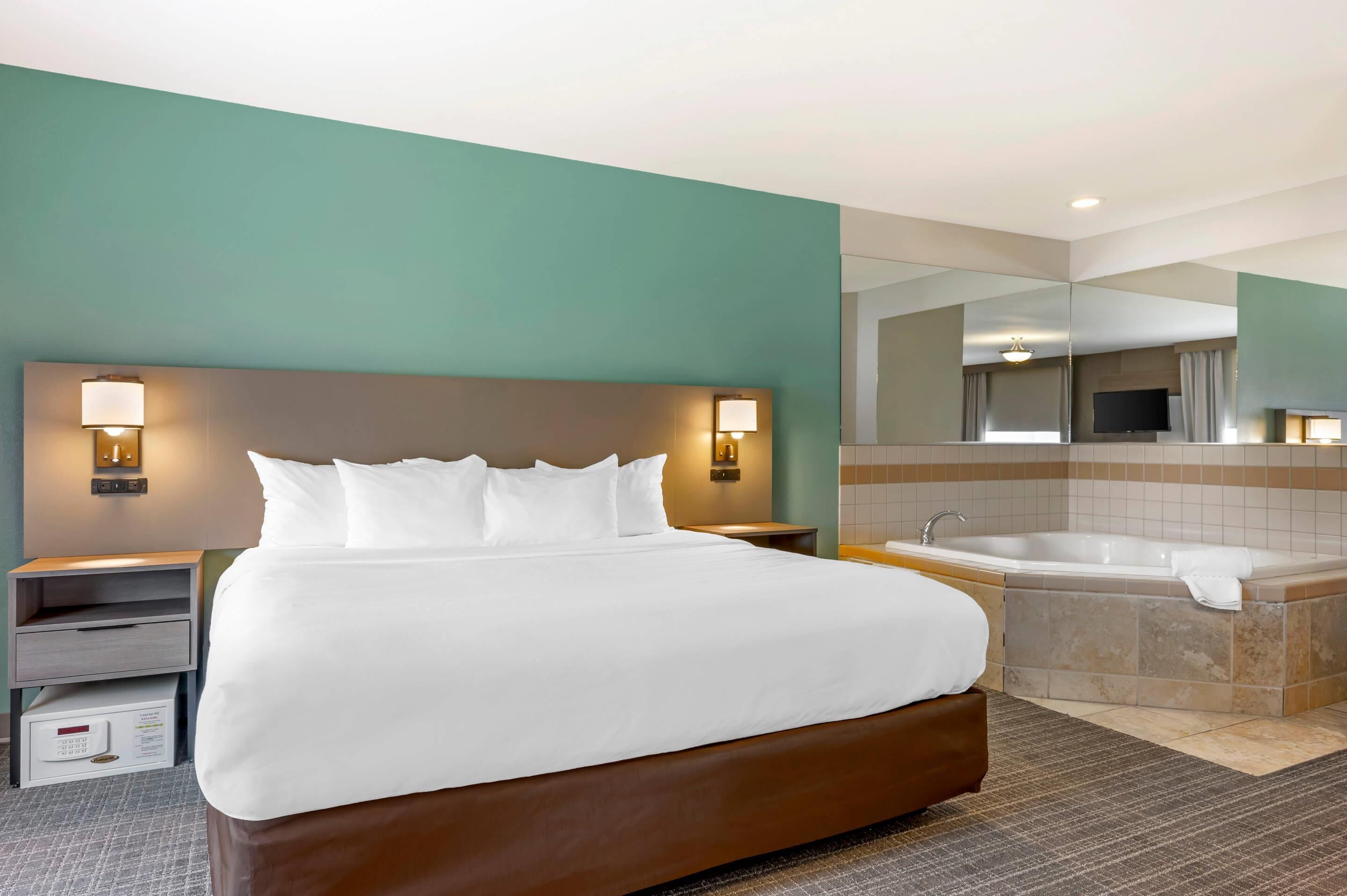 A hotel room with a large bed, a bathroom with a bathtub, and a mirror reflecting the room.