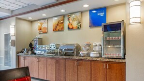A hotel breakfast area with a counter, coffee machines, and a refrigerated display. - Comfort Suites French Lick (French Lick)