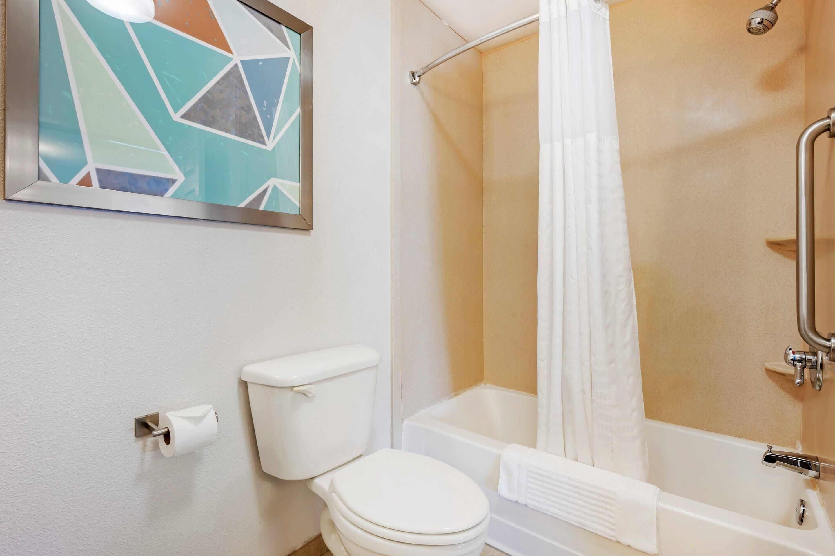 A bathroom with a toilet, a shower with a glass door, and a framed abstract painting on the wall.